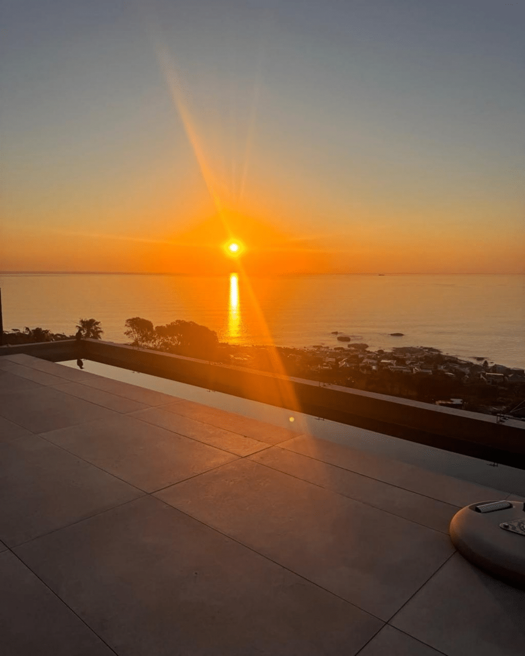 The sun setting over a calm ocean, with soft orange rays of light fanning into the sky and a golden reflection on the water