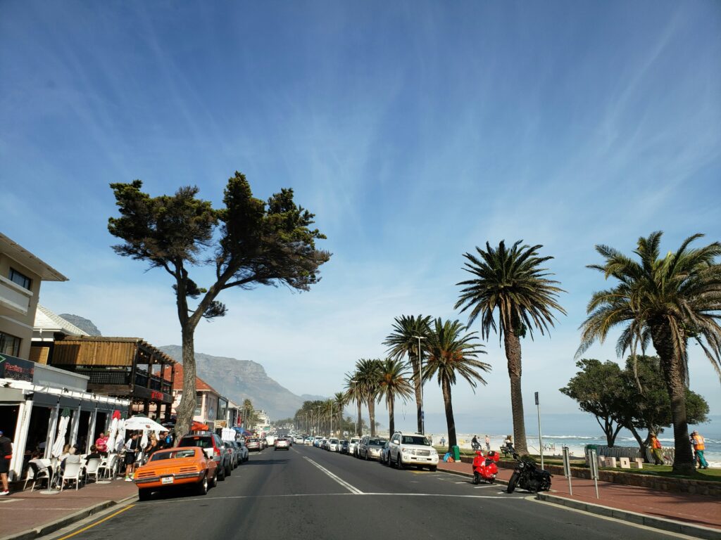 People strolling along the Camps Bay beachfront at dusk with restaurants lit behind them